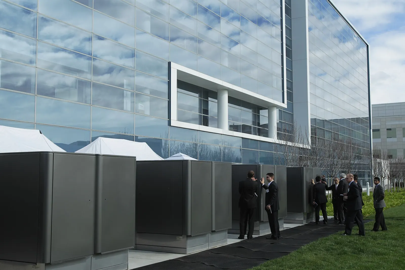 A row of grey cabinet-sized fuel cells beside a glass office building