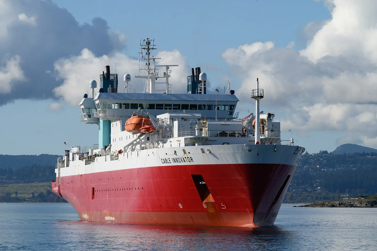 A red and white cable-laying ship arriving in port