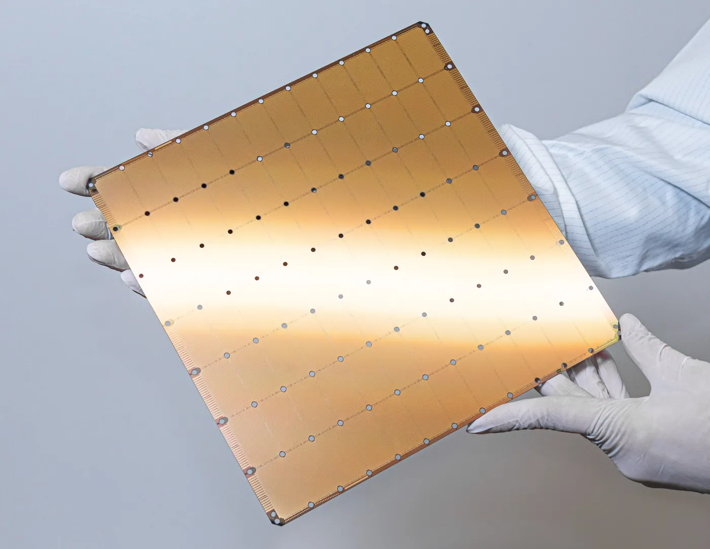 Gloved hands holding a square, gold-coloured wafer-scale processor