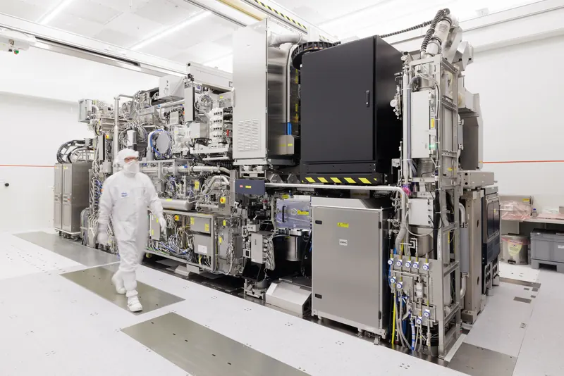 A large EUV lithography machine in a white cleanroom with a technician walking past