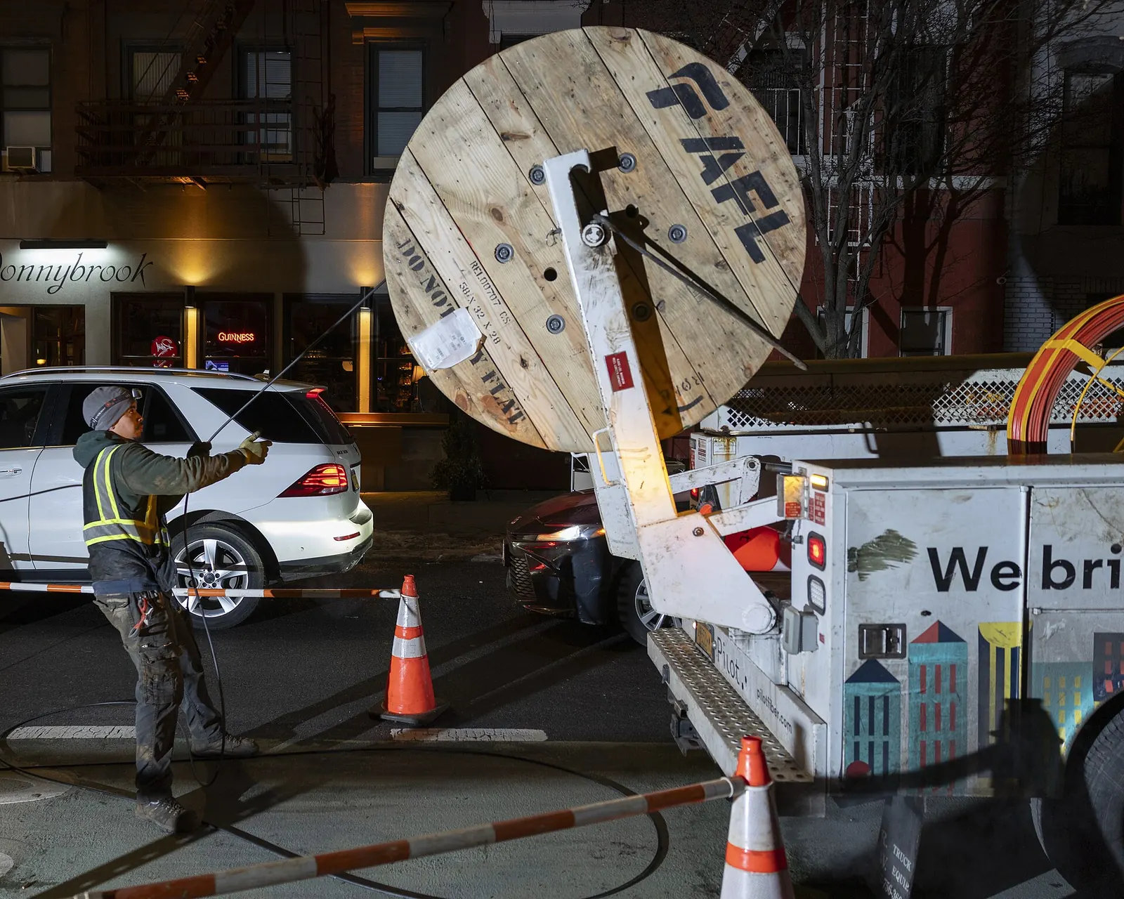 A worker guides fibre-optic cable from a large reel on a truck
