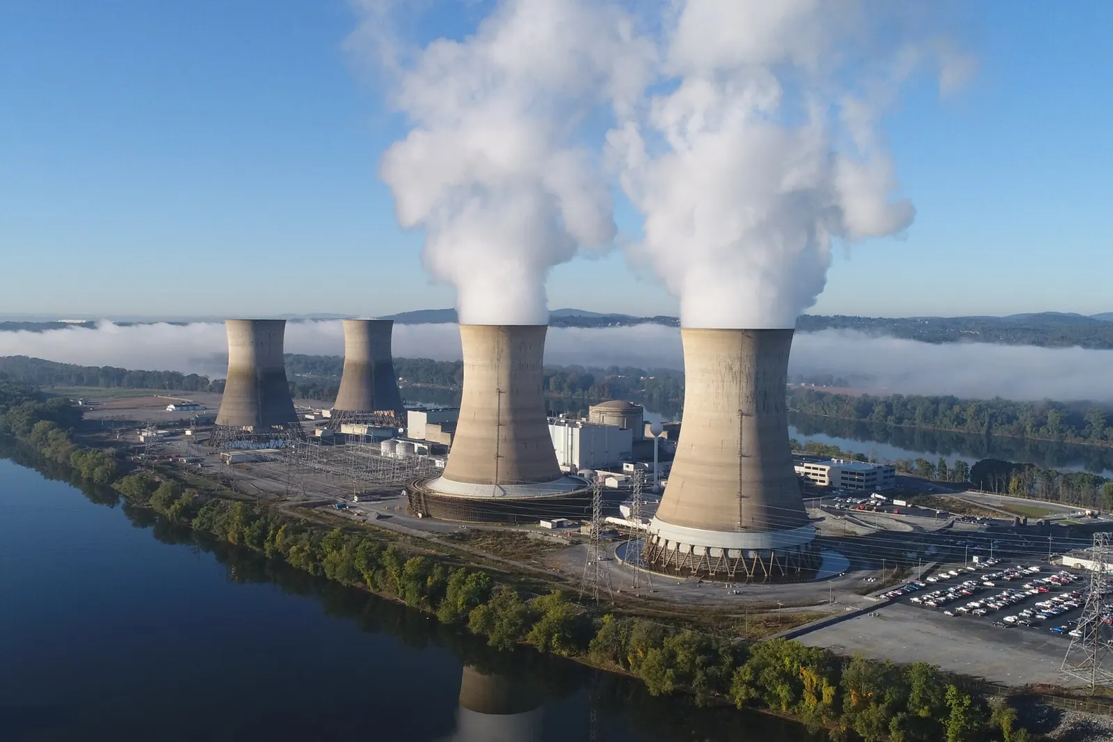 Nuclear cooling towers on a river island, two of them releasing steam