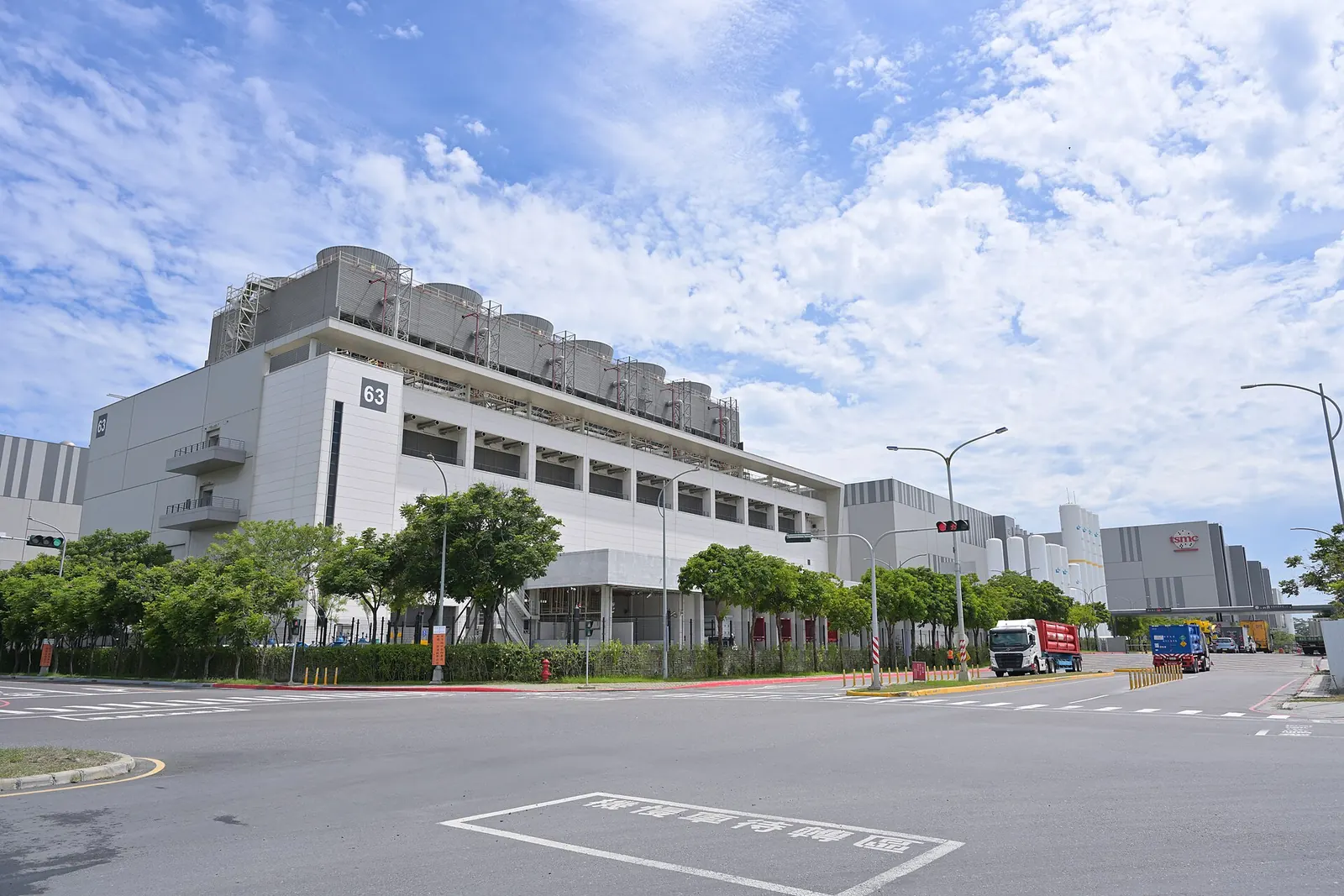 A long, low factory building behind a road and trees