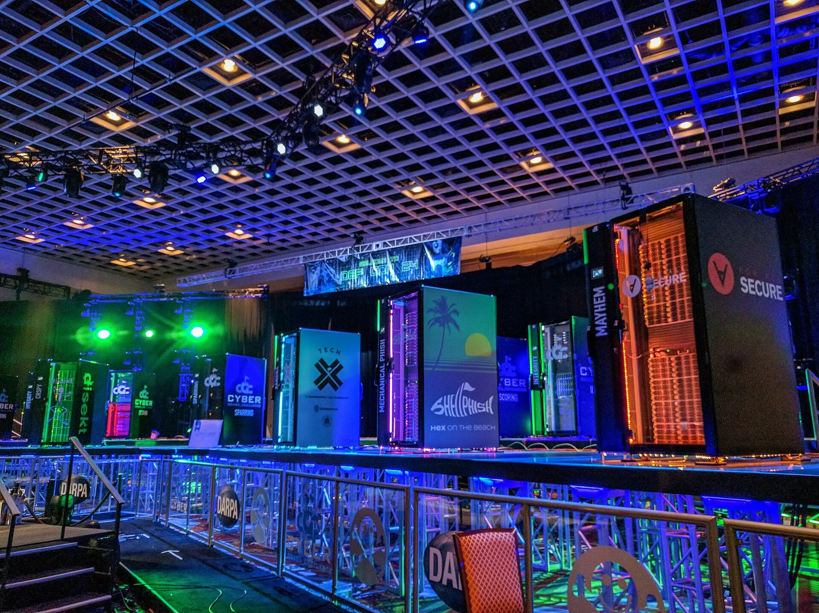 Rows of brightly lit server racks on a stage in a darkened conference hall