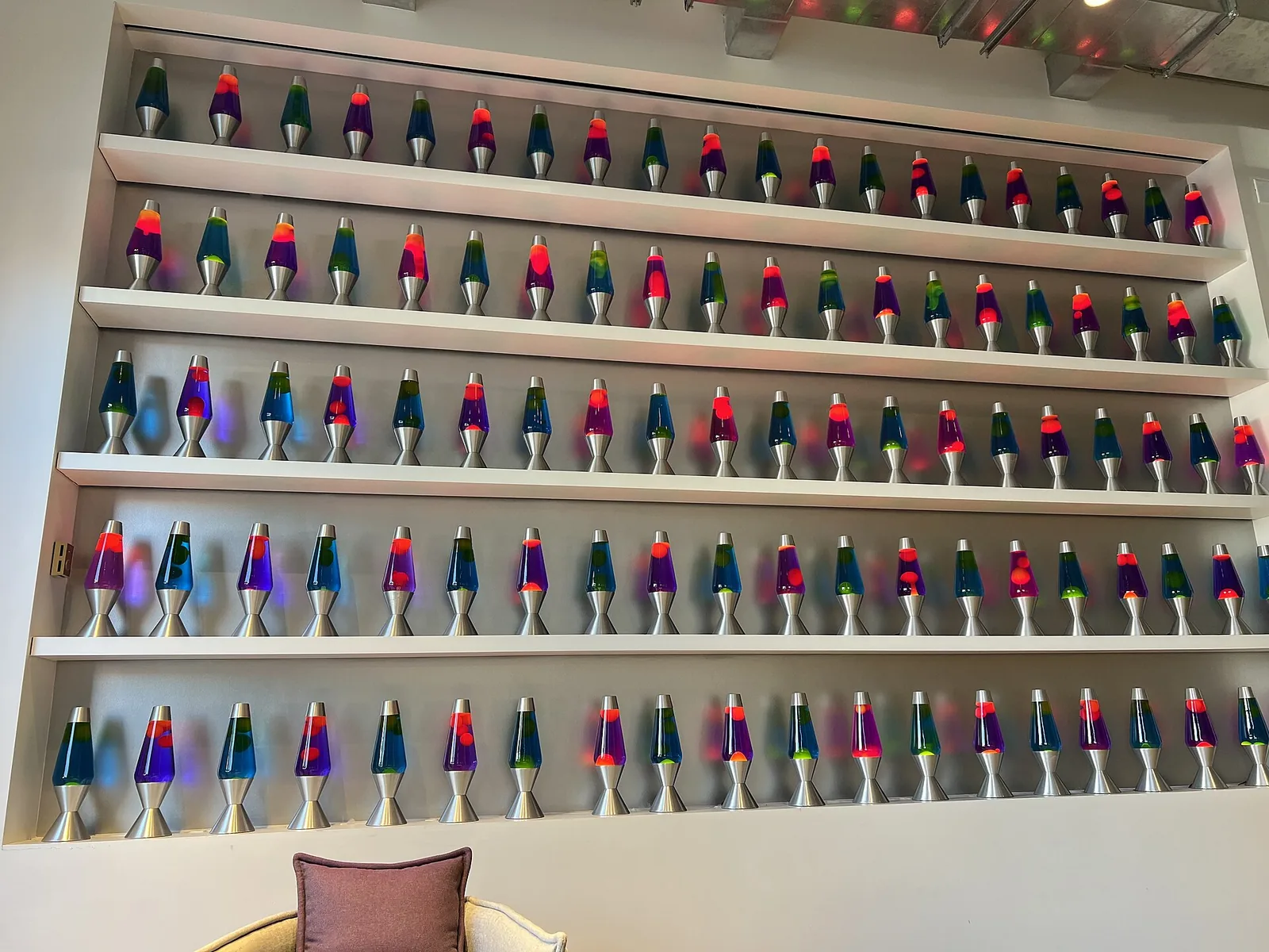 Five shelves of colourful lava lamps along an office wall