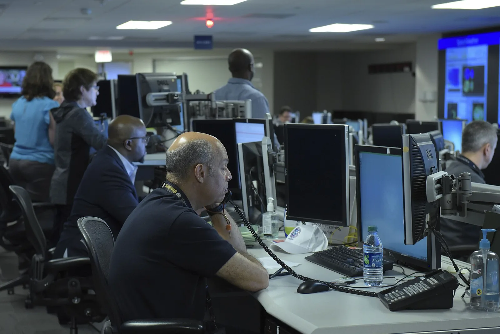 Analysts at desks with several monitors each, in front of a wall of large screens
