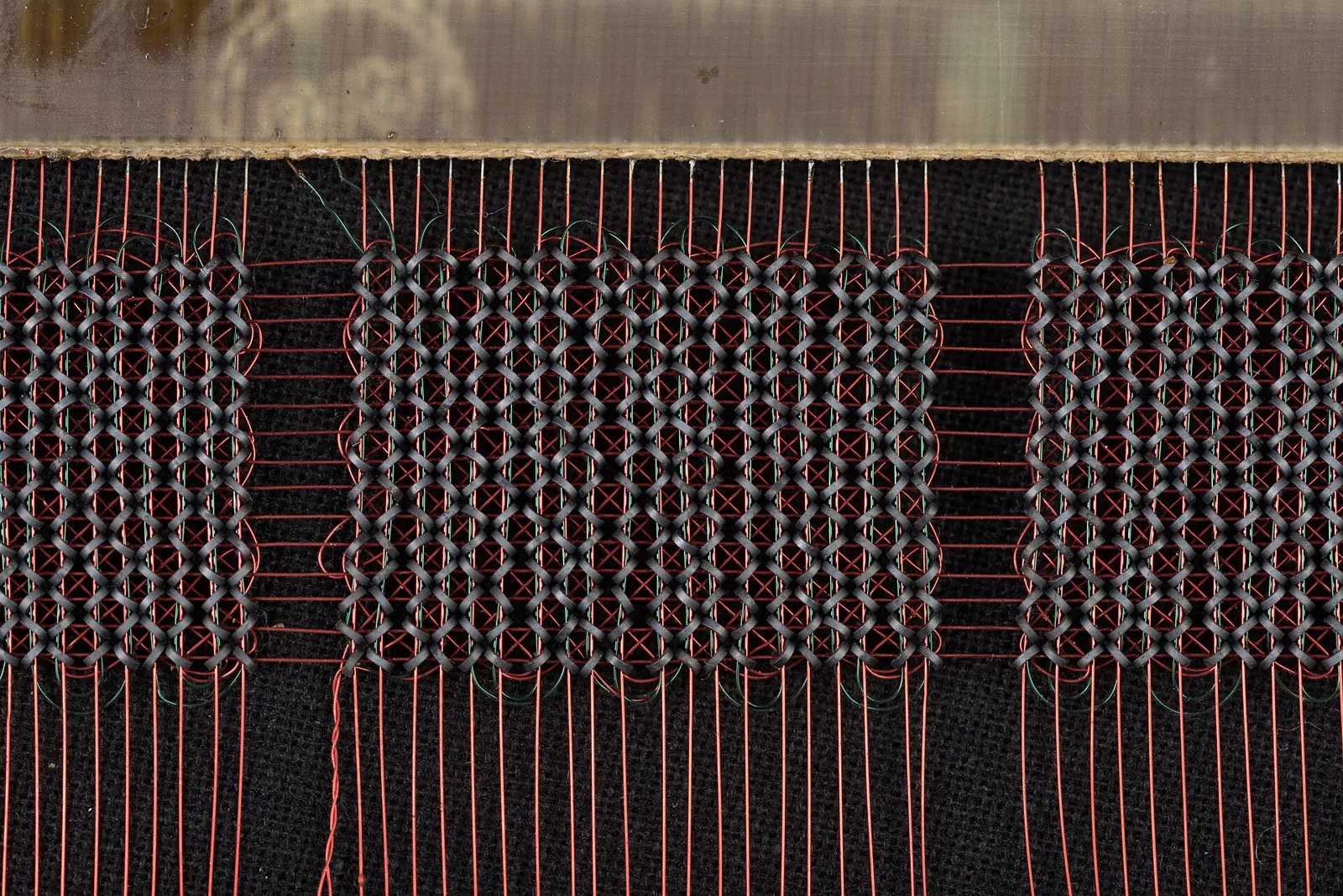 A close-up of a grid of tiny ferrite rings threaded with fine copper wires