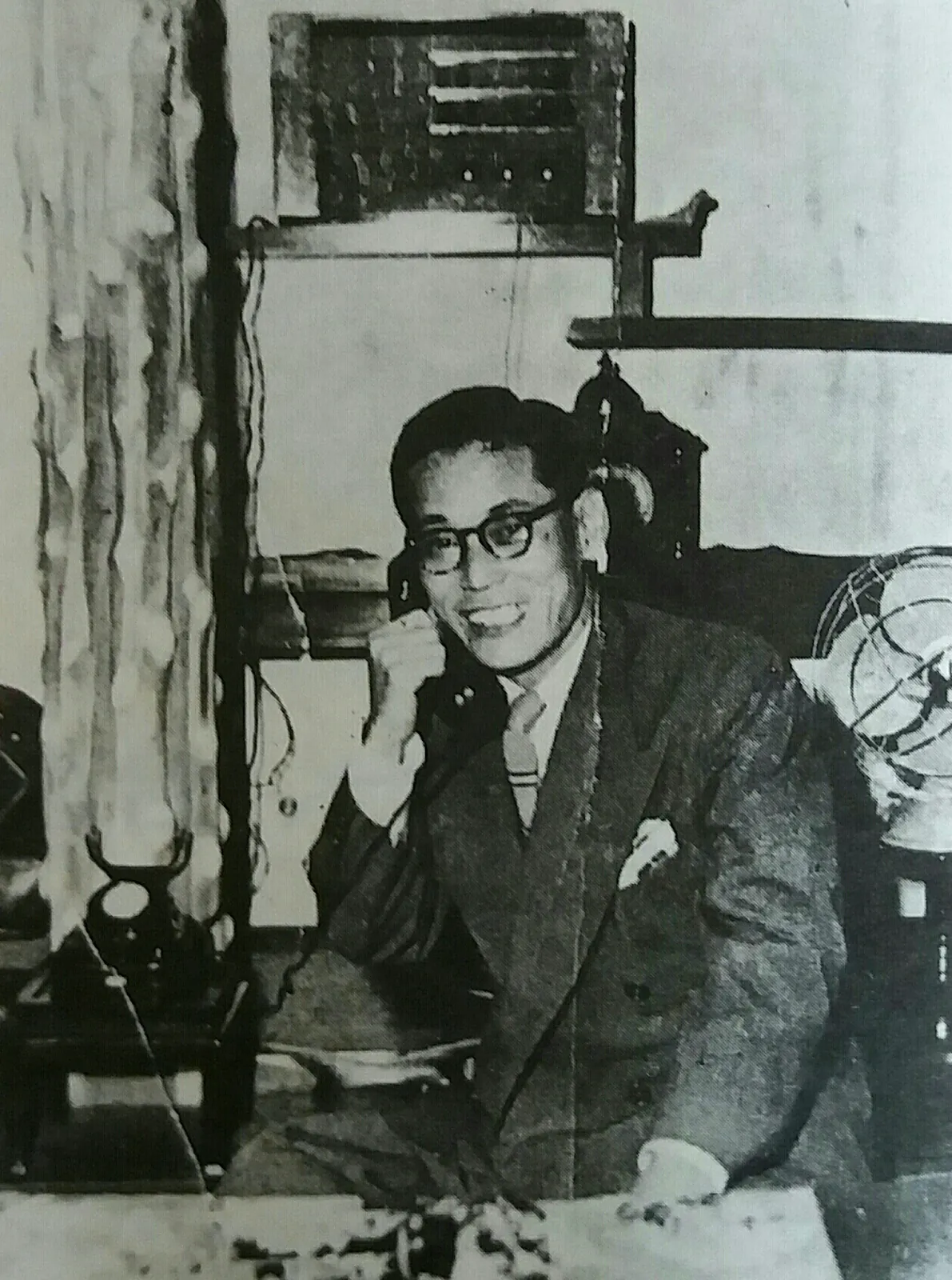 A black-and-white photograph of a man in a suit and glasses at a desk