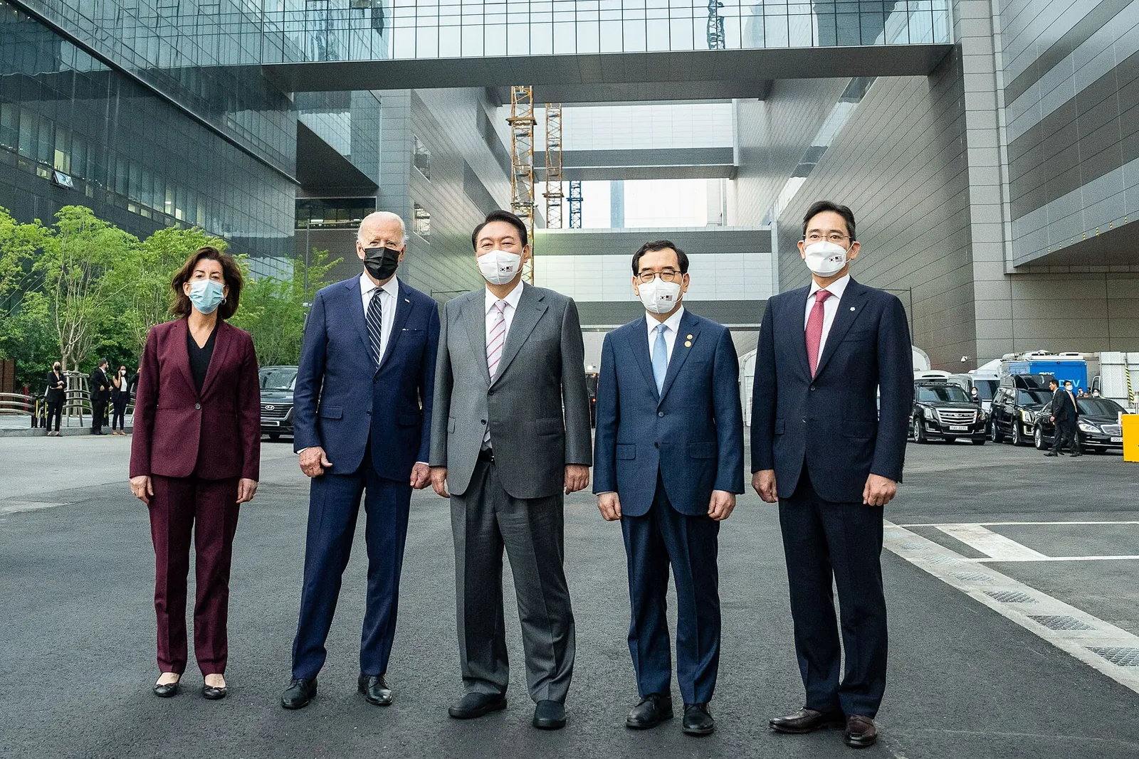 Five people in suits standing in the courtyard of a large glass factory complex